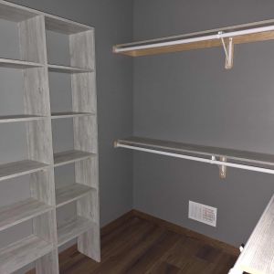 Custom walk-in closet organization system with white built-in shelving and hanging rods in a new master suite.