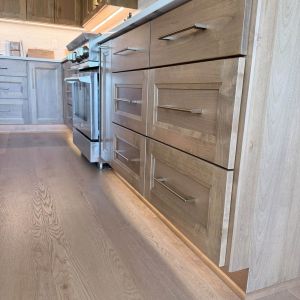 Custom warm wood lower cabinetry with modern drawer pulls and clean white countertops in kitchen remodel by Elite Home Renovations.
