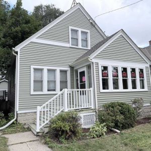 Updated home front exterior featuring new sage green siding, energy-efficient windows, and crisp white trim.   